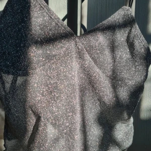 Glittrig linne-topp med smala axelband - Säljer en glittrig linne-topp i silver med smala axelband och v-ringning. Toppen har en croppad passform och är perfekt för att sticka ut. Materialet är syntet och ger ett snyggt skimmer i ljuset.