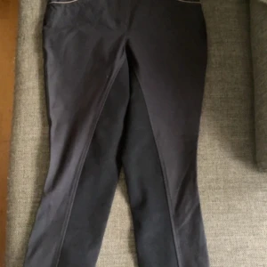 Marinblåa ridbyxor från CRW Classic Riding Wear - Säljer ett par marinblåa ridbyxor från CRW Classic Riding Wear. Byxorna har förstärkta partier på insidan av benen och dekorativa sömmar samt knappar med CRW-logga. Perfekta för ridning och har en klassisk look. Ljusrosa detaljer vid fickorna. Aldrig använda så i nyskick 