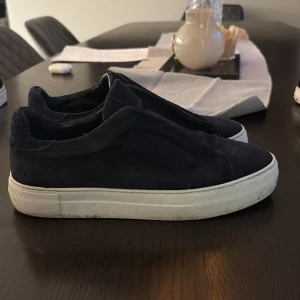 Blåa axel arigatos i bra skick storlek 42 - Säljer ett par svarta sneakers i mocka med stilren design och vit platt sula. Skorna har rund tå och är utan synliga snören för en minimalistisk look. Perfekta för dig som gillar enkel och clean stil Box ingår!!.
