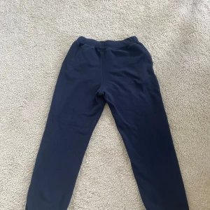 Marinblå mjukisbyxor från Polo Ralph Lauren - Mörkblå mjukisbyxor från Polo Ralph Lauren med resår i midjan och benslut. Klassisk design med diskret logga på ena benet. Perfekta för en avslappnad stil och riktigt sköna att ha på sig.