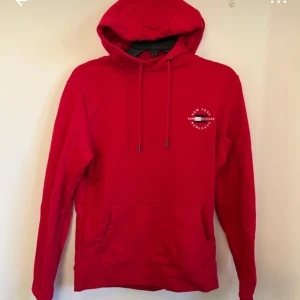 Röd hoodie från Tommy Hilfiger - Säljer en röd hoodie från Tommy Hilfiger med broderad logga och text på bröstet. Tröjan har huva med dragsko och en stor magficka. ANVÄND EN GÅNG, nypris =1100 kr mitt = 149 kr skriv om minsta lilla fundering!