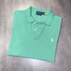 Ralph lauren piké - Snygg grön pikétröja från Polo Ralph Lauren med klassisk passform och vit broderad logga på bröstet. Tröjan har korta ärmar, krage och knäppning med två knappar. Perfekt för en stilren och avslappnad look. Tröjan är i storlek M och passar 165 cm. Tröjan är i bra skick och bara att höra av sig vid funderingar!