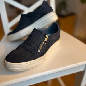 Mörkblå  sneakers med dragkedja och mönstrad yta - Säljer ett par mörkblå  K. Cobler sneakers med vit platt sula och snygg krokodil-liknande struktur. Skorna har en dekorativ dragkedja på sidan , Perfekta för dig som vill ha en unik och stilren look.