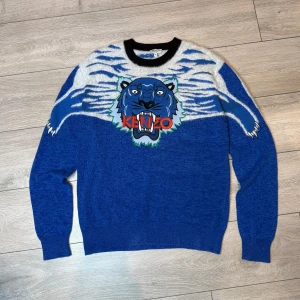 Blå stickad tröja med tiger från Kenzo - Blue Kenzo paris crewneck Elevate Your style and your wardrobe With this limited knitted Blue Kenzo paris crewneck! Condition on this hoodie is 8/10 (a small stitch on the inside of the hoodie but is not visable) 100% authentic. Size M For more information and details feel free to contact us privately!