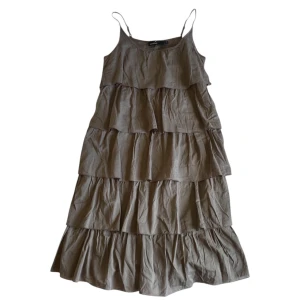 Beige volangklänning med smala axelband - Säljer en beige klänning med flera volanglager och smala axelband. Klänningen har en luftig passform och är perfekt för varma dagar. Tillverkad i ett lätt material som ger en avslappnad känsla.