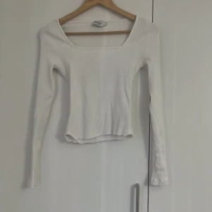 Vit ribbad långärmad topp från NA-KD - Säljer en vit ribbad långärmad topp från NA-KD Reborn. Toppen har en fyrkantig ringning och är figurnära med croppad längd. Perfekt att styla med jeans eller kjol för en trendig look. Den är klippt hemma själv men syns inte så mycket.