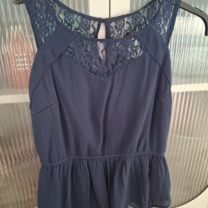 Marinblå topp från Vero Moda - Säljer en marinblå topp från Vero Moda i storlek XS. Toppen har vacker spets upptill både fram och bak, är ärmlös och har en lätt utställd look.. Perfekt för dig som gillar feminina detaljer och en klassisk look.