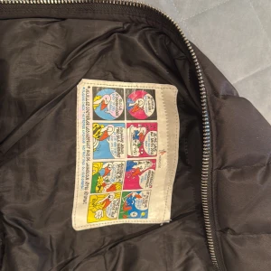  pufferjacka Moncler - Säljer en svart pufferjacka från Moncler med quiltad front och släta ärmar. Jackan har två snedställda fickor med dragkedja, ribbade muddar och en Moncler-logga på ärmen. Perfekt för kyliga dagar.