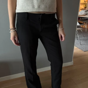 Svarta låg midjade kostymbyxor med normal passform - Snygga svarta kostymbyxor med klassisk rak passform och diskreta fickor bak. Byxorna har hällor för bälte och stängs med dragkedja och knapp framtill. Perfekta till en stilren look.