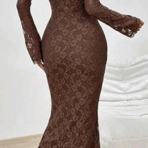 Brun långklänning i spets med blommönster - Säljer en brun långklänning i spets med blommigt mönster. Klänningen har lång ärm och figurnära passform med fyrkantig ringning. Perfekt för dig som vill ha en elegant och unik look.