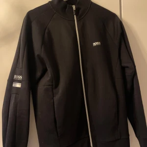 Svart zipjacka från Hugo Boss - Säljer en svart zipjacka från Hugo Boss med diskret logga på bröstet och ärmen. Storlek S i gott skick!