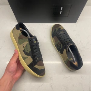Saint Laurent Skor - Camouflage Saint Laurent-skor – Sällsynt modell  Säljer ett par Camouflage färgade sneakers från Saint Laurent i en mycket ovanlig modell som inte tillverkas längre. De är svåra att få tag på och passar perfekt för dig som gillar unika skor.  Storlek 40 EU, men Saint Laurent är oftast lite större i storleken – så de kan passa dig som brukar ha 40.5 också.  Detta ingår:  - Nya reservsnören - Äkthetskort   Skorna är i fläckfritt begagnat skick, finns för upphämtning på Lindholmen utanför Göteborg 