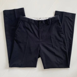 Svarta kostymbyxor med raka ben - Snygga svarta chinos med normal passform och raka ben. Klassisk design med knapp och dragkedja i midjan samt fickor fram och bak. Perfekta för en stilren och enkel look.
