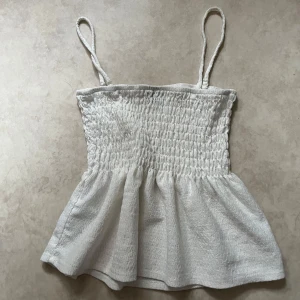 Vit smockad linnetopp från Gina Tricot - Säljer en söt vit linnetopp från Gina Tricot i storlek XXS. Toppen har smockad överdel och tunna axelband, samt en lätt utställd nederdel. Perfekt för varma dagar och enkel att matcha med jeans eller kjol. Använt ett par gånger men passar även till XS personer! Tar gärna prisförslag om det låter rimligt!🥰