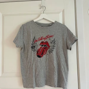 Grå Rolling Stones t-shirt från Vila - Säljer en grå t-shirt från Vila med Rolling Stones-tryck framtill. T-shirten har klassisk passform, korta ärmar och är gjord i mjuk bomull. Perfekt för dig som gillar bandtröjor och vill ha en cool vardagsstil. PRIS GÅR ATT DISKUTERAS
