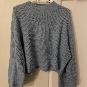 Ljusblå stickad tröja - Mysig ljusblå stickad tröja med breda ärmar. Perfekt för lager-på-lager och passar till både jeans och kjol. Tröjan har en hög ribbad krage och grovstickat mönster. Även perfekt att ha över kanske ett linne en sommarkväll! 