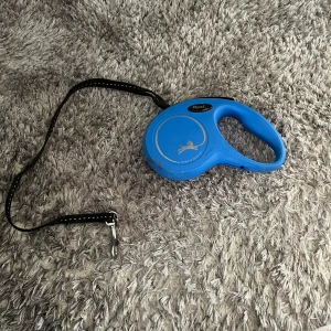 Blå Flexi hundkoppel - Säljer ett blått Flexi hundkoppel med svart band och reflexdetaljer. Handtaget är ergonomiskt utformat för ett bekvämt grepp och kopplet har en metallkrok för enkel fastsättning i halsband eller sele.