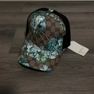 Keps från Gucci - Exklusiv Gucci keps i en unik blommig design med klassiska GG-monogrammet i bakgrunden. Kepsen är väldigt stilren och svår att få tag på. Tillverkad i högkvalitativa material med skön passform. Helt oanvänd och i nyskick. PERFEKT FÖR SOMMARN SOM ÖR RUNT HÖRNET!