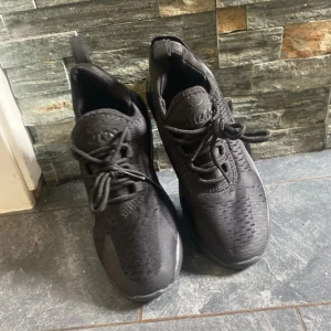 Svarta Nike sneakers - Säljer ett par helsvarta Nike sneakers med snörning och rund tå. Skorna har en sportig design med ventilerande mesh och platt sula. Perfekta för träning eller vardagsstil.