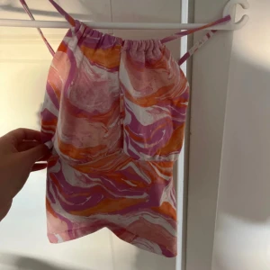 Färgglad mönstrad linnetopp - Säljer en färgglad linnetopp med abstrakt mönster i rosa, orange och vitt. Toppen har smala axelband som korsas i ryggen. Perfekt för varma dagar!