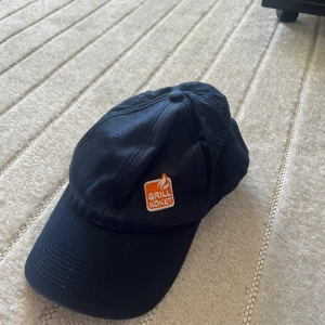Mörkblå keps från 7-Eleven med Grillköket-logga - Mörkblå keps med böjd skärm och justerbar baksida. Framtill sitter en orange och vit broderad patch med texten 'Grillköket'. Kepsen är märkt med 7-Eleven på insidan och har klassisk passform.