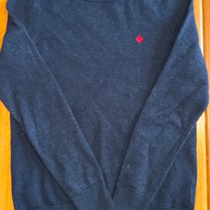 Mörkblå tröja från Morris - Säljer en stilren mörkblå tröja från Morris med ett rött emblem på bröstet. Tröjan har långa ärmar och en rund halsringning. Perfekt för en klassisk och avslappnad look. Obs sitter inte som s sitter som xs. Hör av er vid frågor!