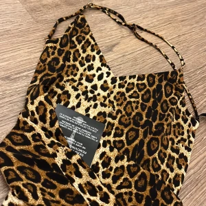 Leopardmönstrad klänning från NLY One - Snygg leopardmönstrad klänning från NLY One med smala axelband och en figurnära passform. Perfekt för en djärv look. Klänningen har en v-ringad design och är tillverkad i ett mjukt material.