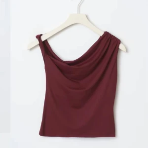 Vinröd oneshoulder topp - Snygg vinröd oneshoulder topp med draperad design. Perfekt för en stilren look. Tillverkad i mjukt material som ger en bekväm passform. Endast använd en gång