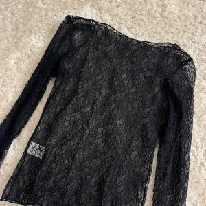 Svart spets topp - Elegant svart spets topp med långärmad design. Perfekt för en stilfull look med sitt genombrutna mönster och mjuka material.