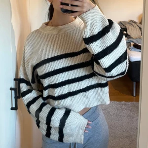 Beige och svart randig stickad tröja från NA-KD - Säljer en beige stickad tröja med svarta ränder. Tröjan är croppad och har långa ärmar. Perfekt för en avslappnad stil.