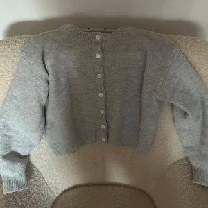 Grå stickad kofta med knappar - Säljer en mysig ljusgrå/grå stickad kofta med knappar hela vägen fram. Koftan har långa ärmar och ribbade muddar vid ärmslut och nederkant. Tröjan är väldigt mjuk och i ull. Köpt på plick så vet ej varumärket (lappen är klippt). Den är i storlek s men sitter som xs. Använt fåtal gånger. 😊