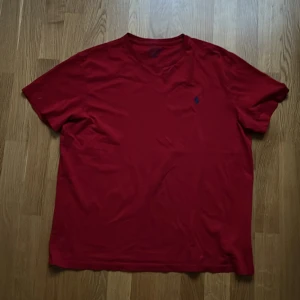 Röd t-shirt från Ralph Lauren - Snygg röd t-shirt från Ralph Lauren med en liten broderad logga på bröstet. Perfekt för en stilren och avslappnad look. Tillverkad i mjukt bomullsmaterial för extra komfort.