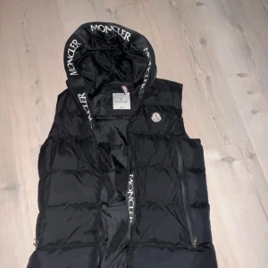 Svart dunväst från Moncler - Snygg svart dunväst från Moncler med huva och dragkedja. Storlek M säljer den eftersom jag inte vill ha den längre knappt använd. Perfekt för kyliga dagar.