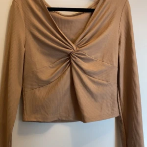 Beige ribbad topp med knutdetalj - Snygg beige ribbad topp med långärmad design och en elegant knutdetalj framtill. Perfekt för en stilren look den är i ny skick från Shein i storlek S.