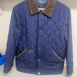 Blå quiltad jacka från Polo Ralph Lauren -  Säljer en stilren och klassisk Ralph Lauren jacka i storlek Junior L.  Jackan har  bra skick och har inte använt många gånger 
