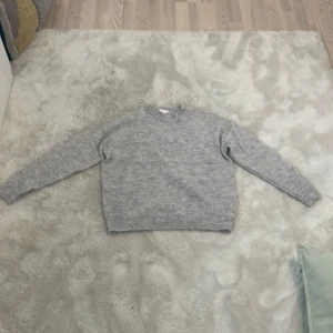 Grå stickad tröja från Gina Tricot - Säljer en mysig grå stickad tröja från Gina Tricot. Perfekt för kyliga dagar med sin mjuka och bekväma passform. Tröjan har långa ärmar och ribbade kanter vid ärmslut och nederkant. Passar utmärkt för både höst och vinter.