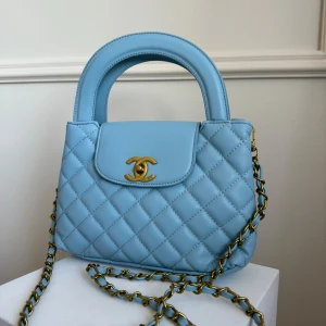 Blå lyxig  väska  - Ny och oanvänd! Elegant blå quiltad handväska med gulddetaljer och kedja. Väskan har ett klassiskt märke på framsidan och en praktisk handrem. Perfekt för att ge en lyxig touch till din outfit. Längd 23cm höjd 26cm