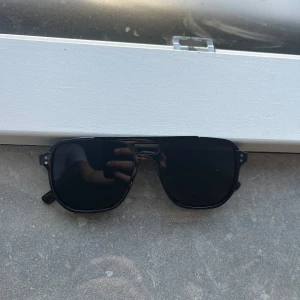 Svarta solglasögon - Snygga svarta solglasögon med rektangulära linser och en stilren design. Perfekta för en snygg look i solen. De har en solid svart ram och mörka linser som ger ett klassiskt intryck.