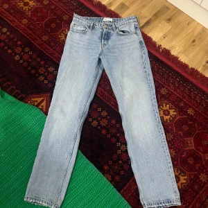 Ljusblå jeansbyxor - Säljer ett par klassiska ljusblå jeansbyxor med knappgylf och raka ben. De har en traditionell femficksdesign och är perfekta för en avslappnad stil. Jeansen har en snygg, sliten look vid fållen. De är jätte fina 