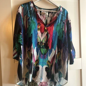 Färgglad blus från By Malina - Säljer en färgglad blus från By Malina med ett unikt mönster i blått, grönt och rött. Blusen har trekvartsärmar och en lös passform, perfekt för en somrig look. Den är tillverkad i ett lätt och luftigt material.