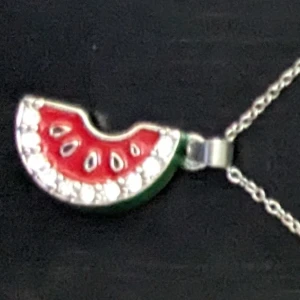 Halsband med vattenmelonhänge - Charmigt halsband med ett färgglatt vattenmelonhänge. Hänget är dekorerat med röda, gröna och vita detaljerr. Perfekt för att ge en lekfull touch till din stil. Passar barn och ungdomar perfekt. Till vuxen blir det ett kort halsband.