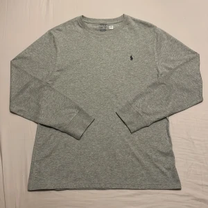  Polo Ralph Lauren Långärmad tröja - Säljer en stilren grå långärmad tröja från Polo Ralph Lauren. Tröjan har en klassisk passform med det ikoniska broderade logotypen på bröstet. Perfekt för en avslappnad och snygg look. Endast använd en gång. Säljer på grund av att den var för stor. Priset är inte skrivet i sten!
