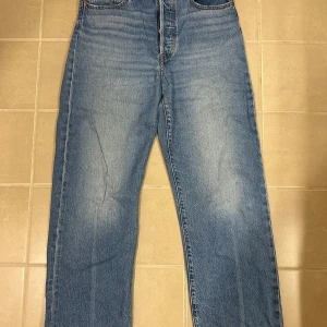 Levi's Ribcage Straight Jeans - Säljer ett par klassiska Levi's Ribcage Straight jeans i en snygg blå tvätt. De har en hög midja och raka ben, vilket ger en tidlös look. Perfekta för en avslappnad stil.