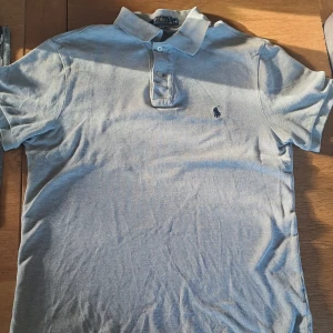 Grå pikétröja från Ralph Lauren - Snygg grå pikétröja från Ralph Lauren med klassisk krage och knappslå. Den har en broderad logotyp på bröstet och korta ärmar.   Den har storlek M men har slimfit