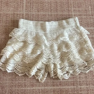 Vita spets shorts - Säljer ett par vita shorts med  spetsdesign och volanger. De är ett par shorts som du kan välja lågmidjade och högmidjade men jag föredrar låg midjade.perfekta för sommarens varma dagar. Passar bra till en avslappnad stil eller en mer uppklädd look.