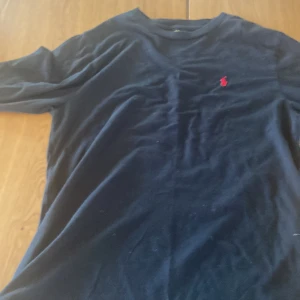 Svart långärmad tröja från Polo Ralph Lauren - Säljer en klassisk svart långärmad tröja från Polo Ralph Lauren med det ikoniska röda logotypbroderiet på bröstet. Perfekt för en stilren och avslappnad look.