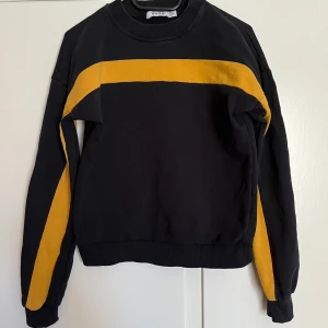 Svart tröja med orange detalj - Säljer en svart tröja med orangea detaljer från NA-KD. Tröjan har tyvärr en liten fläck som ej syns så mycket men annars är den i bara bra skick