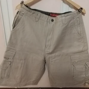 Beige cargo shorts med fickor - Snygga beige cargo shorts med flera praktiska fickor och bälteshällor. Perfekta för en avslappnad stil. De har en knapp och dragkedja framtill. Vintage Abercrombie Fitch Baggy Cargo Pants T-2083 Beige Paratroopers Mens M- Cargo Lagom används då och då. I väldig bra skick. Förvarad i klädskåp. Inga fel eller blekningar, fläckar eller likadana övergripande täcken på användning!
