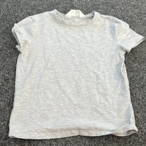 Grå t-shirt från H&M - Säljer en enkel och stilren grå t-shirt från H&M. Den är kortärmad och gjord i mjukt bomullsmaterial, perfekt för vardagsbruk. Passar bra till jeans eller shorts för en avslappnad look.
