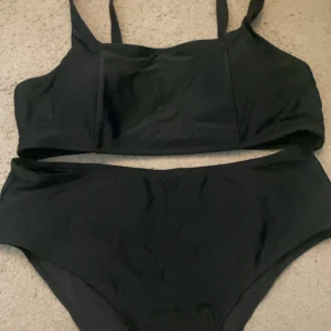 Svart bikini med justerbara axelband - Snygg svart bikini med justerbara axelband och en stilren design. Toppen har en enkel och bekväm passform med en praktisk spänne baktill. Perfekt för en dag på stranden eller vid poolen.